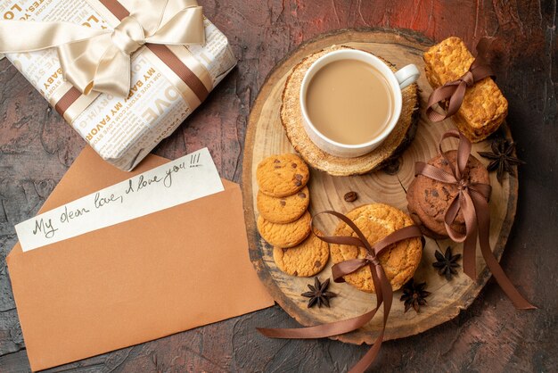 Vista superior sabrosas galletas atadas con cuerda taza de café en tablero de madera carta de amor en sobre de regalo en la mesa