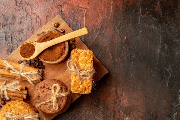 Vista superior sabrosas galletas atadas con granos de café de cuerda en un tazón de canela sobre tablero de madera en la mesa oscura