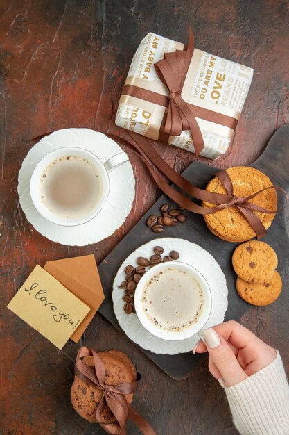 Vista superior sabrosas galletas con tazas de café y presente sobre fondo oscuro galleta dulce té pareja amor color pastel mañana