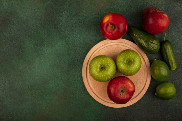 Foto gratuita vista superior de sabrosas manzanas rojas y verdes en una tabla de cocina de madera con limones, aguacate y pepino aislado en una pared verde con espacio de copia