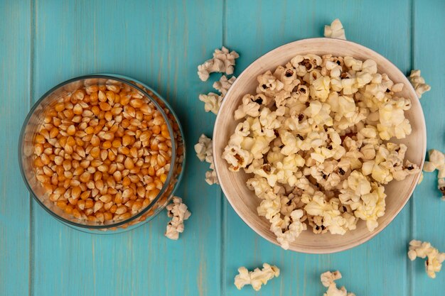 Vista superior de sabrosas palomitas de maíz en un recipiente con granos de palomitas de maíz en un frasco de vidrio sobre una mesa de madera azul