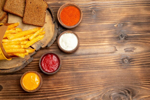 Vista superior de sabrosas papas fritas con condimentos en mesa marrón