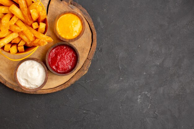 Vista superior de sabrosas papas fritas con salsas en mesa negra