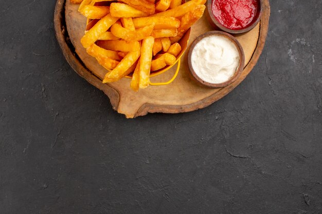 Vista superior de sabrosas papas fritas con salsas en negro