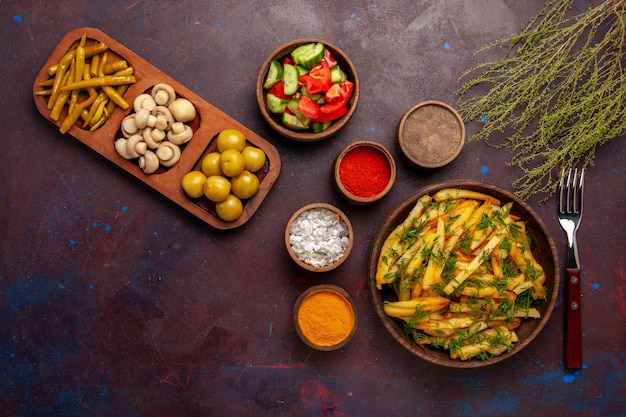 Vista superior sabrosas papas fritas con verduras y diferentes condimentos en el escritorio oscuro