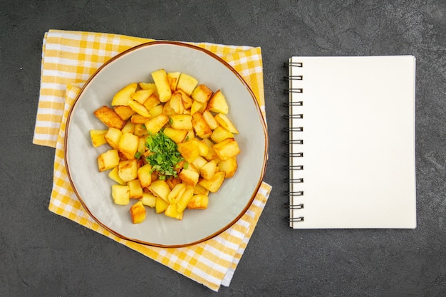 Vista superior de sabrosas patatas fritas dentro de la placa con el bloc de notas en la superficie gris oscuro