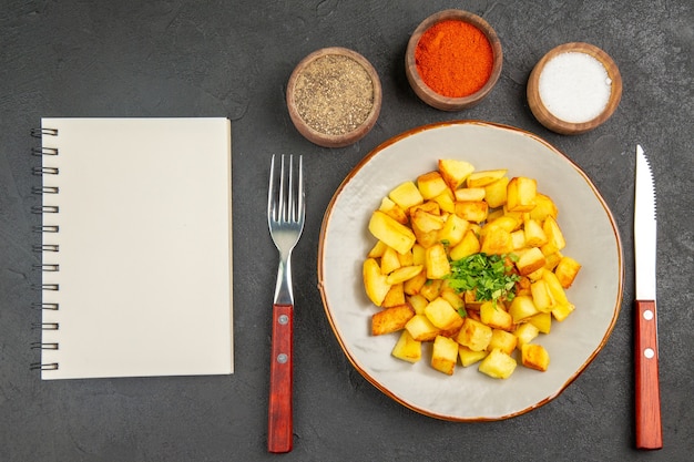 Foto gratuita vista superior de sabrosas patatas fritas dentro de la placa con condimentos en la superficie oscura