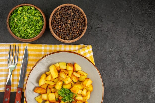 Vista superior de sabrosas patatas fritas dentro de la placa con verduras en la superficie gris oscuro