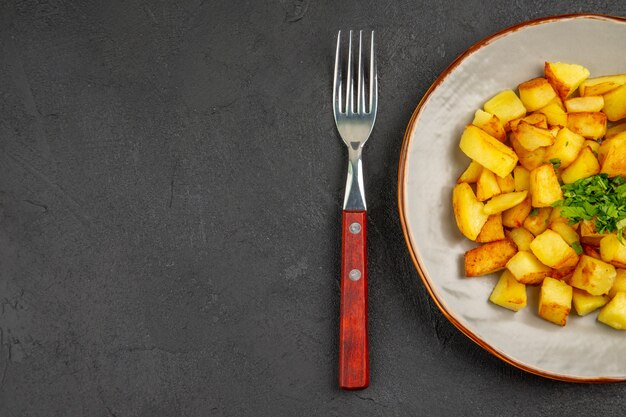 Vista superior de sabrosas patatas fritas dentro de la placa con verduras en la superficie oscura