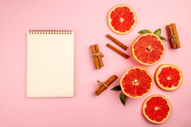 Vista superior de sabrosas rodajas de fruta de pomelos con canela en la superficie rosa