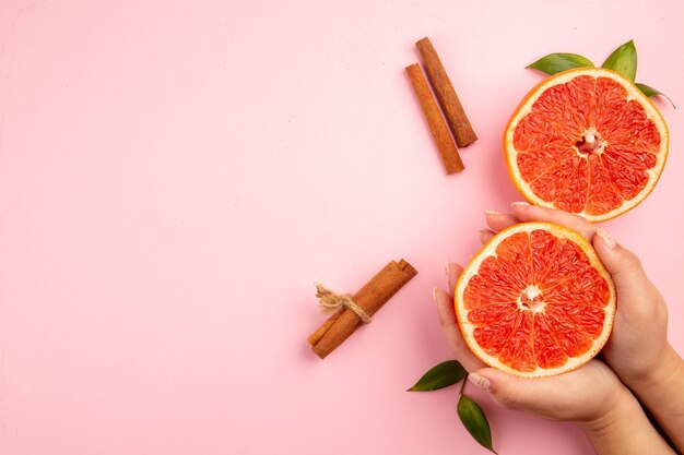 Vista superior de sabrosas rodajas de fruta de pomelos con canela en la superficie rosa