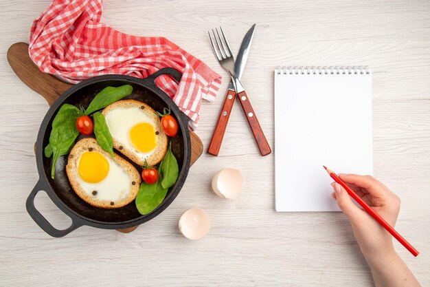 Vista superior sabrosas tostadas de huevo dentro de la sartén con huevos frescos sobre fondo blanco pan color almuerzo plato desayuno comida té