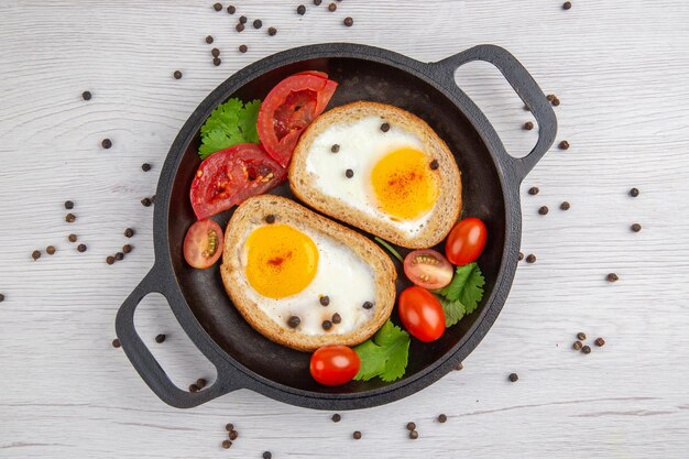 Vista superior sabrosas tostadas de huevo con tomates dentro de la sartén sobre fondo blanco desayuno almuerzo color ensalada comida comida