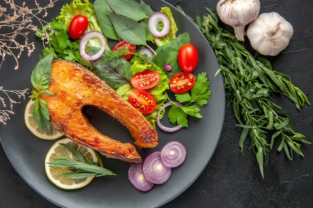 Vista superior sabroso pescado cocido con verduras frescas y condimentos en la mesa oscura