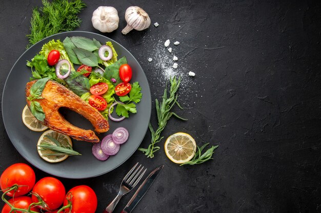 Vista superior sabroso pescado cocido con verduras frescas en la mesa oscura