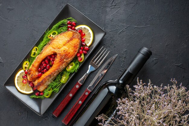Vista superior sabroso pescado cocido con verduras y rodajas de limón dentro de la sartén en la mesa oscura