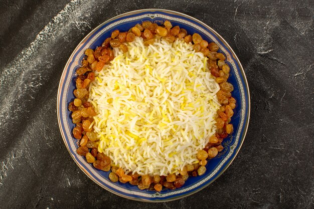 Una vista superior sabroso pilaf con aceite y pasas secas dentro de la placa en la superficie oscura