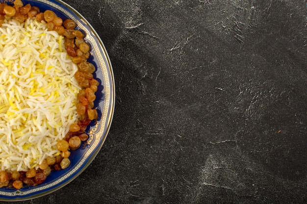 Una vista superior sabroso pilaf con aceite y pasas secas dentro de la placa en la superficie oscura