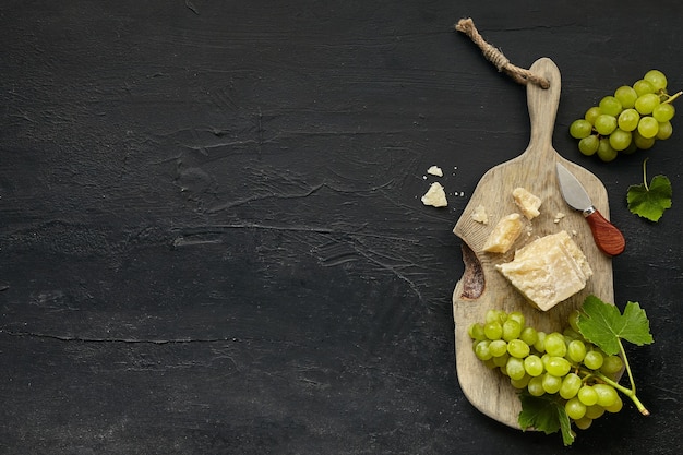 Vista superior del sabroso plato de queso con fruta, uva en un plato de cocina de madera sobre el fondo de piedra negra