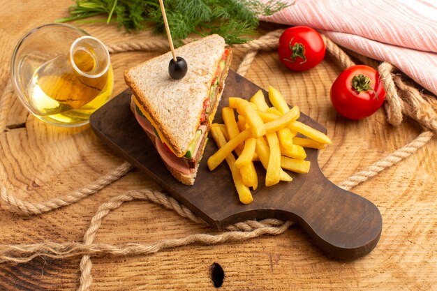 Vista superior sabroso sándwich con jamón de oliva tomates verduras junto con papas fritas cuerdas aceite tomates rojos en el fondo de madera sándwich comida merienda desayuno