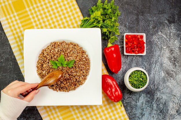 Vista superior sabroso trigo sarraceno cocido con verduras y pimientos en la mesa gris claro