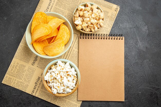 Vista superior de sabrosos chips de queso con diferentes bocadillos para el tiempo de la película en el fondo oscuro