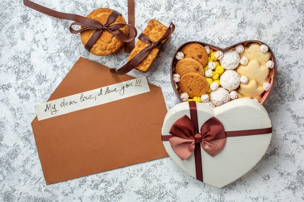 Vista superior de sabrosos dulces, galletas, galletas y caramelos dentro de una caja en forma de corazón sobre fondo blanco, té de azúcar, dulce y delicioso pastel.