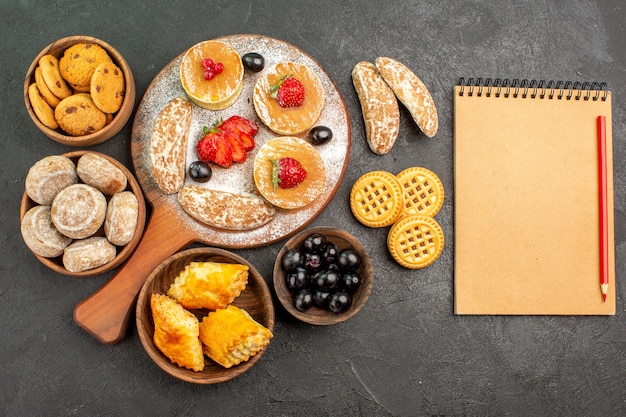 Vista superior sabrosos panqueques con diferentes dulces en el postre de pastel de azúcar de escritorio oscuro