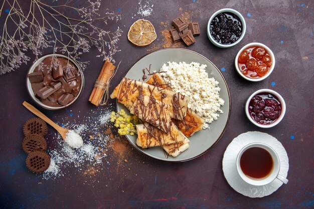 Vista superior de sabrosos pasteles dulces con taza de té y requesón sobre fondo oscuro, pastelería, pastel de galletas, azúcar, té dulce