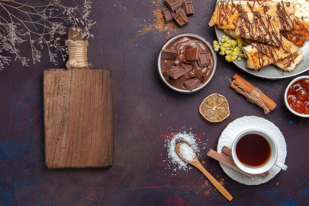 Vista superior sabrosos pasteles dulces con taza de té sobre fondo oscuro pastelería pastel de galletas azúcar postre de té dulce