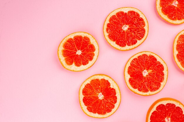 Vista superior de sabrosos pomelos en rodajas de frutas jugosas forradas en la superficie rosa