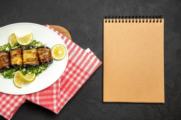 Vista superior de sabrosos rollos de berenjena plato cocido con rodajas de limón en la superficie oscura cena aceite cocinar comida plato cítrico