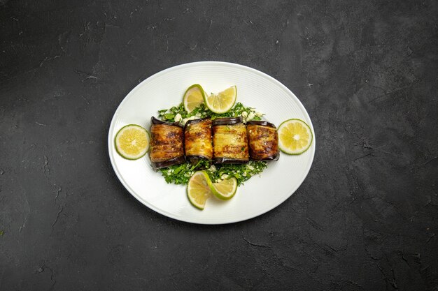 Vista superior de sabrosos rollos de berenjena con rodajas de limón en la superficie oscura plato de cena de comida de cocina de fruta