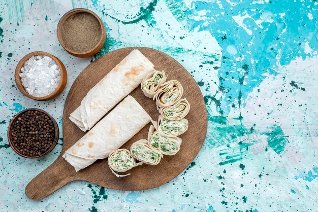 Vista superior sabrosos rollos de vegetales enteros y en rodajas con verduras y condimentos en el fondo azul rollo de comida comida color vegetal