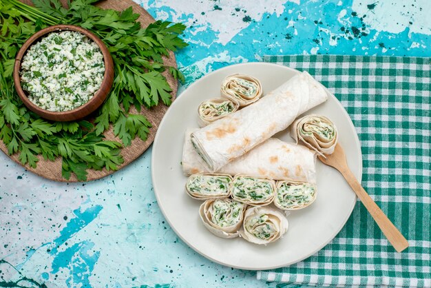 Vista superior sabrosos rollos de verduras enteras y en rodajas con verduras y ensalada en la mesa azul comida comida rollo color vegetal