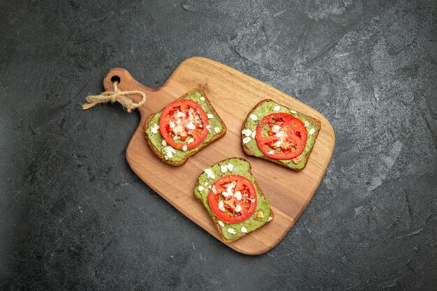 Vista superior sabrosos sándwiches de aguacate con tomates rojos en rodajas en el bocadillo de pan de sándwich de hamburguesa de fondo gris