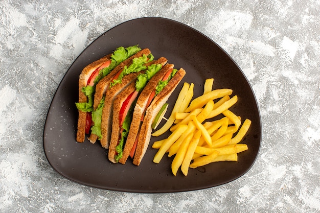 Vista superior de sabrosos sándwiches con ensalada de tomates verdes junto con papas fritas dentro de un plato oscuro