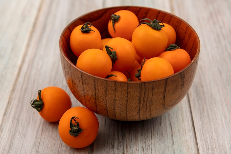 Foto gratuito vista superior de sabrosos tomates cherry anaranjados en un cuenco de madera sobre una pared de madera gris