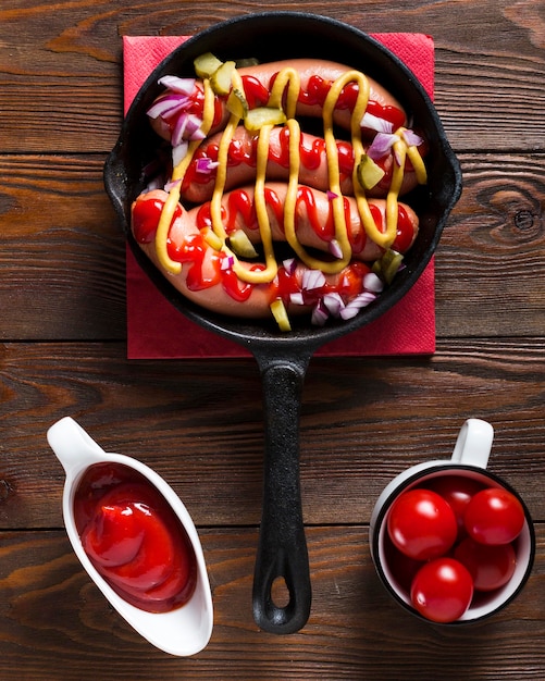 Vista superior de salchichas en sartén con salsas y tomates cherry