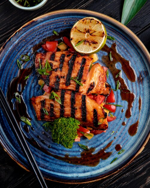 Vista superior de salmón a la plancha con verduras limón y salsa de soja en un plato sobre la mesa de madera