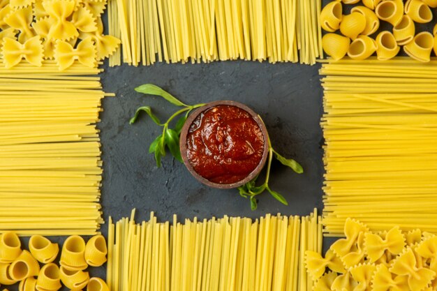 Vista superior de salsa de tomate con pasta cruda y espagueti en forma de decoración