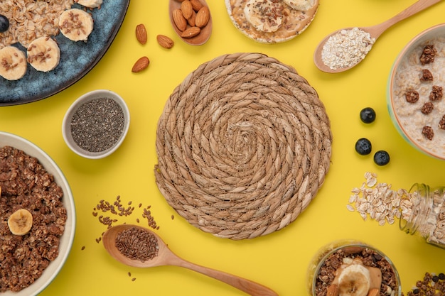 Vista superior del salvamanteles con plátano endrino avena plátano pan crujiente bocadillo plátano nuez y avena con leche de nuez y batido de plátano con semillas de chía cucharas llenas de lino de almendras sobre fondo amarillo