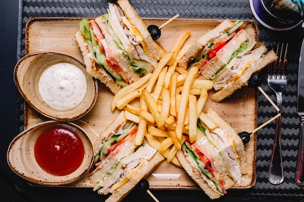 Vista superior del sándwich club servido con papas fritas, salsa de tomate y mayonesa