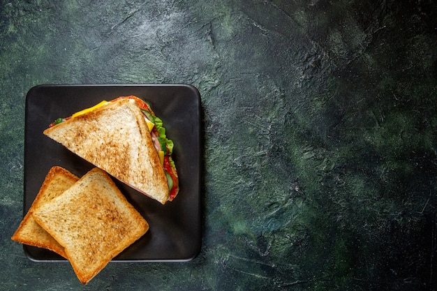 Vista superior de sándwiches de jamón con tostadas dentro de la placa sobre una superficie oscura