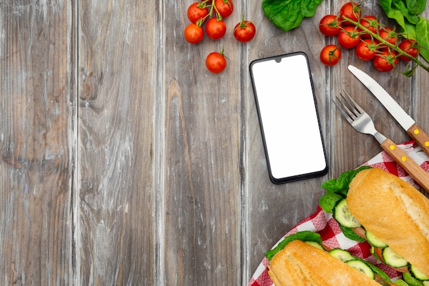 Vista superior de sándwiches con tomate y teléfono inteligente