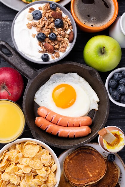Vista superior de la sartén con huevo y salchichas rodeadas de comida para el desayuno