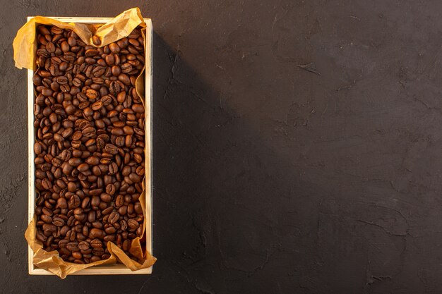 Una vista superior de las semillas de café marrón dentro de la caja sobre el fondo oscuro taza de café foto semillas bebida