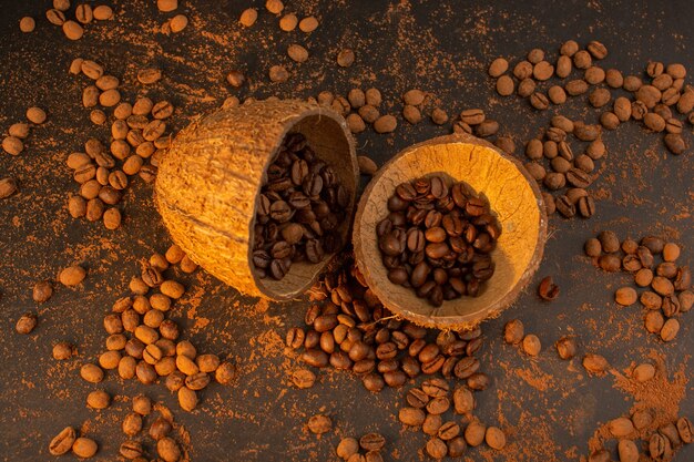 Una vista superior de las semillas de café marrón dentro y fuera de las cáscaras de coco en el escritorio marrón gránulo de grano de semilla de café