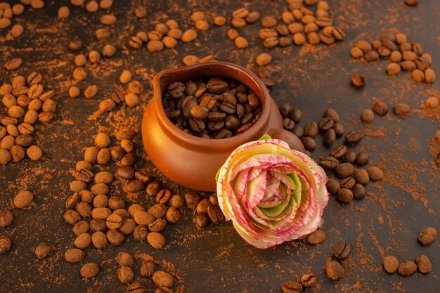 Una vista superior de semillas de café marrón dentro de una jarra marrón con flor y por todo el cuadro marrón