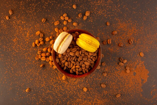 Una vista superior de semillas de café marrón dentro de la placa marrón con macarons franceses en la mesa marrón